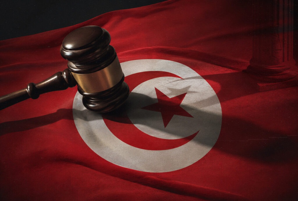 Tunisian flag beside a judge’s gavel and wooden sound block, symbolising Tunisia’s judiciary and Article 86 cases.